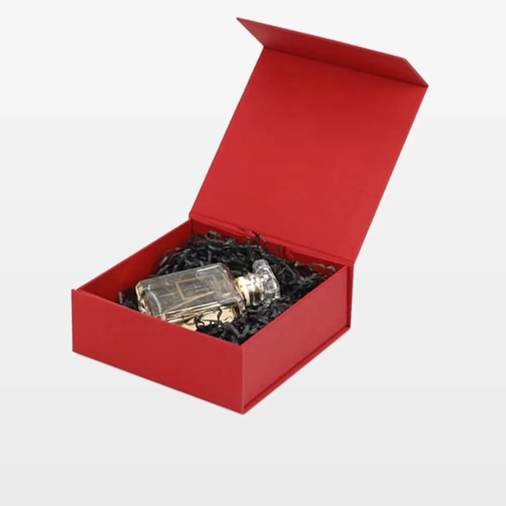 جعبه کتابی مگنتی قرمز باز با شیشهٔ عطر روی پوشال کاغذی مشکی